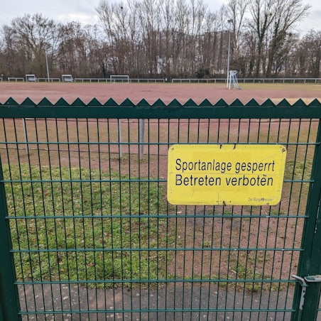 Das Foto zeigt ein Schild „Sportanlage gesperrt. Betreten verboten“ am Tor zum Tennenplatz an der Buschstraße.