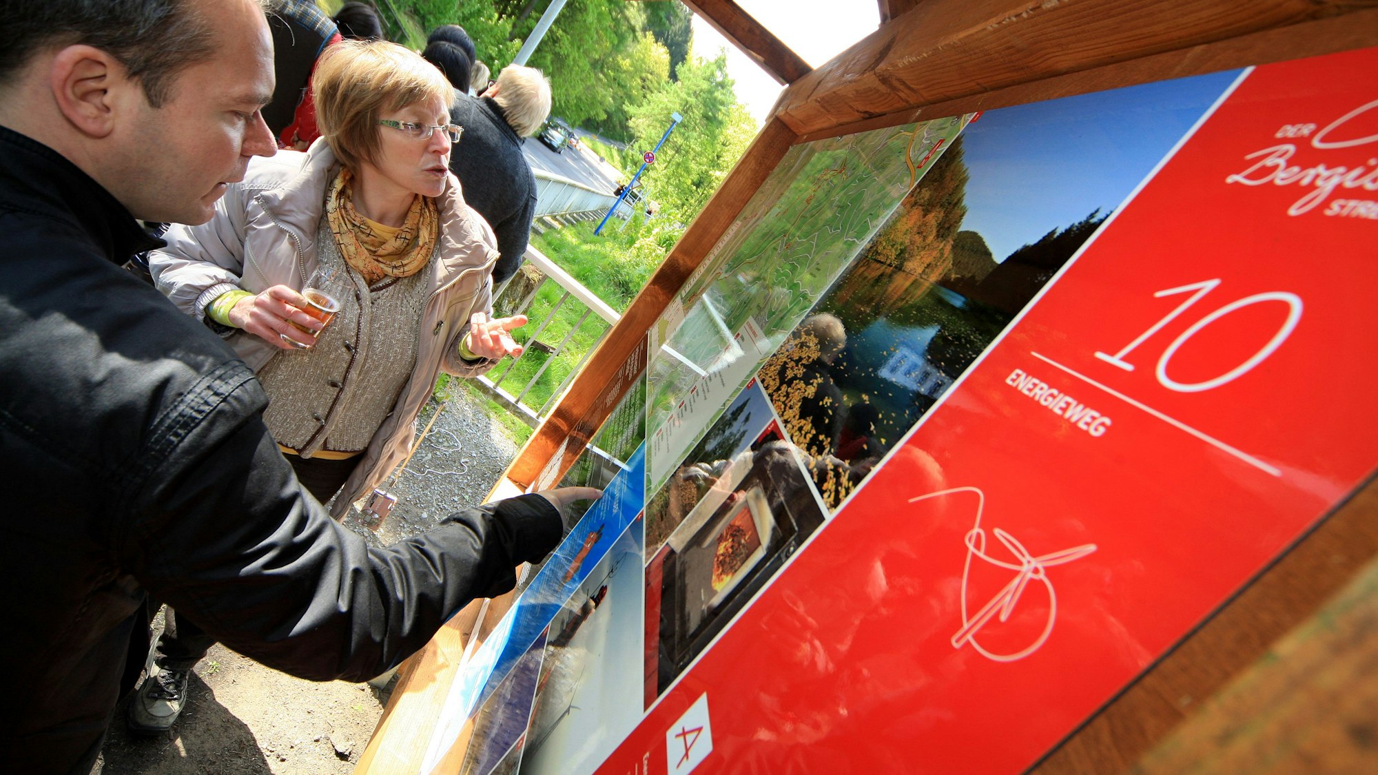 Menschen schauen auf die Start/Ziel-Tafel des Energiewegs bei Gummersbach auf dem Parkplatz an der Aggertalsperre.