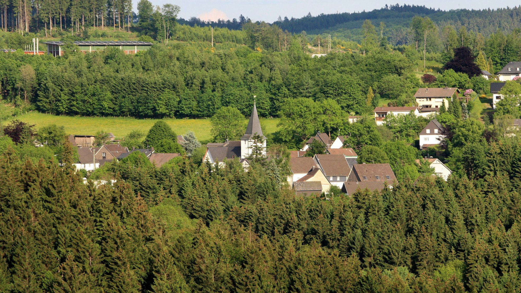 Zwischen Bäumen und Wiesen ist ein Dorf mit Kirche zu sehen.