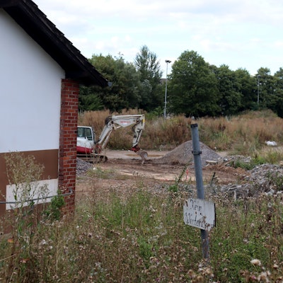 Der Sportplatz in Bad Münstereifel besteht aus Geröllhaufen und ist zugewuchert. Im Hintergrund steht ein Bagger, im Vordergrund ist das schon vor der Flut nicht mehr nutzbare Vereinsheim zu sehen, daneben steht ein Schild mit dem Hinweis „Kein Winterdienst“.
