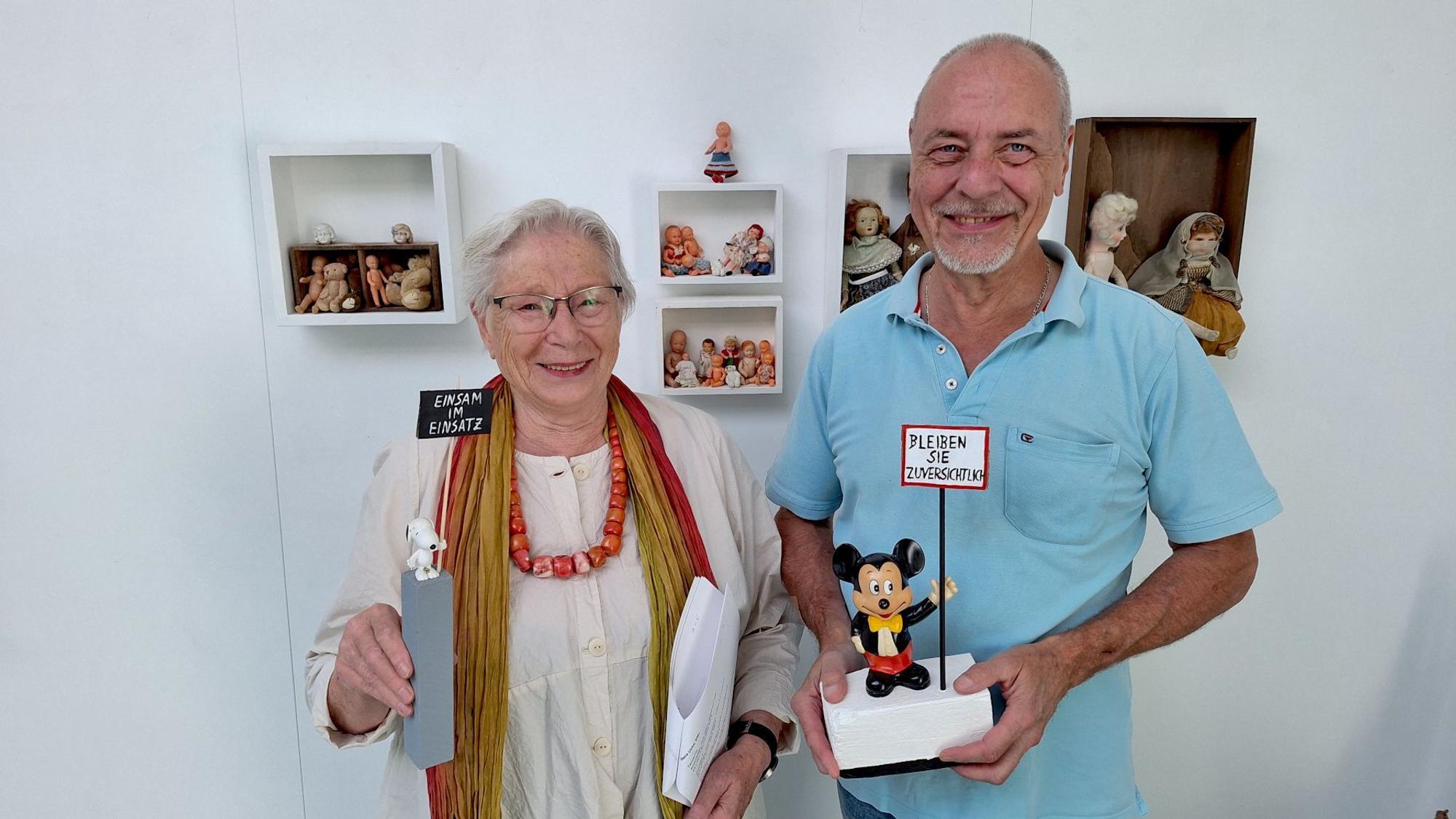 Die Kuratorin und der Geschäftsführer stehen vor Wandkästen und halten Ausstellungsstücke in den Händen.