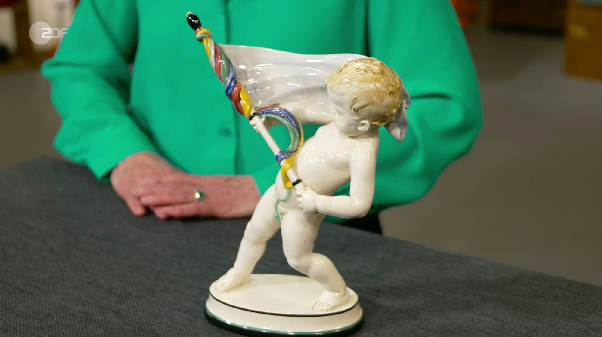 Als weiteres Objekt der Sendung wurde ein Fahnenträger aus Keramik von Friederike Werner der Manufaktur Karlsruher Majolika zugeschrieben. Sie datierte den Putto von Gestalter Arnim Müller auf 1913. Der Wunschpreis lag bei 300 Euro, die Expertise nur bei 180 bis 200 Euro. Händler Ferdinand Resul Adanir zahlte aber 420 Euro. (Bild: ZDF)