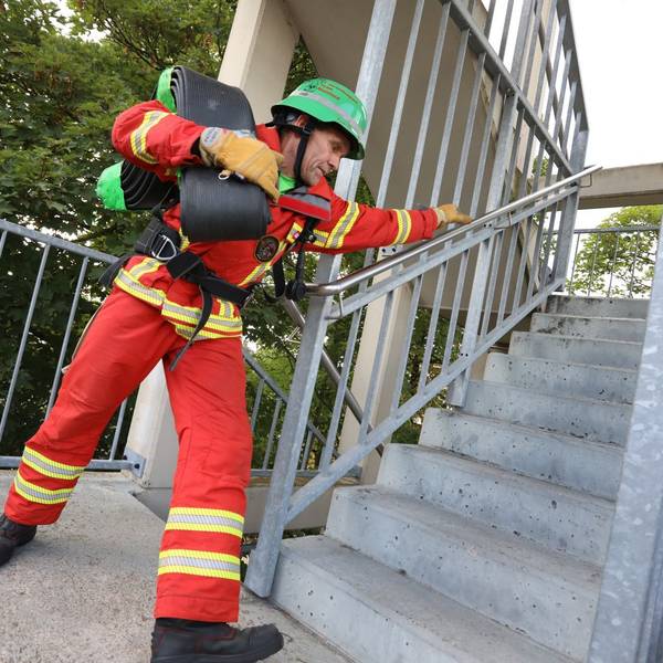 Ein Mann in roter Kleidung und mit grünem Helm läuft eine Treppe hinauf.
