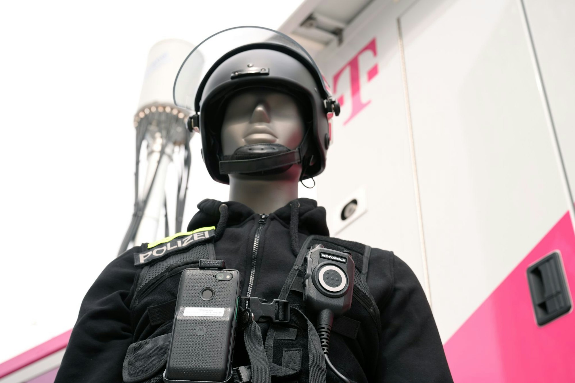 Eine Puppe in Polizei-Uniform zeigt, wie es gehen soll: An ihrer Uniform ist nicht nur ein Funkgerät, sondern auch ein Smartphone befestigt. Die Einsatzzentrale kann sich auf das Smartphone schalten und dank der Kamera sehen, was gerade los ist.