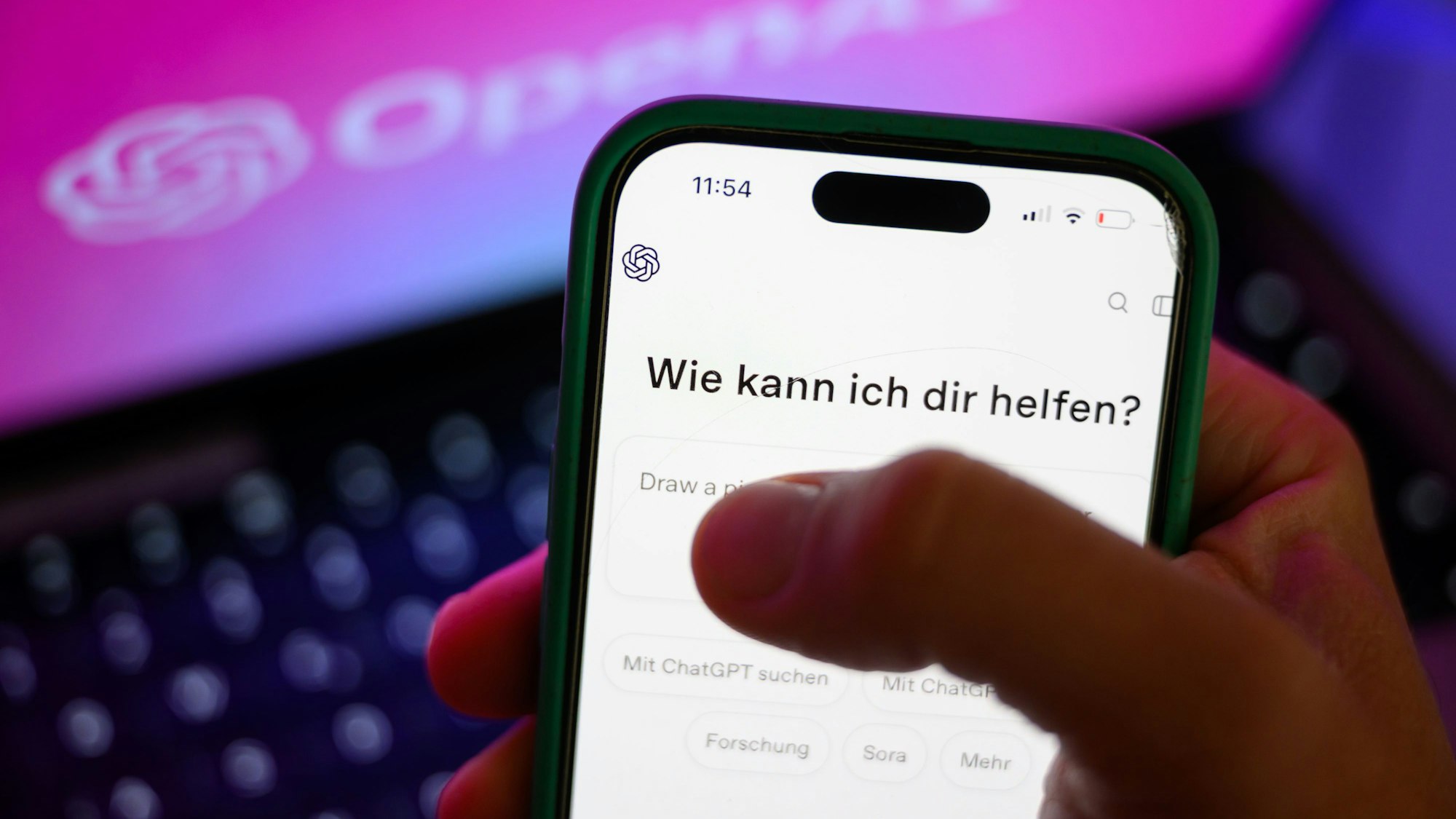 Ein Smartphone mit dem KI-Chatbot ChatGPT ist vor dem Logo des US-Softwareunternehmens OpenAI zu sehen.