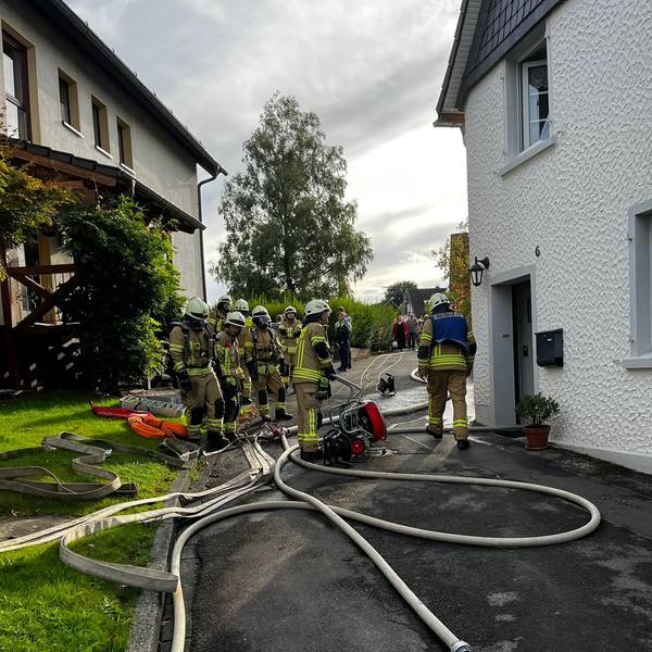 Mehrere Feuerwehrleute stehen vor einem Wohnhaus.