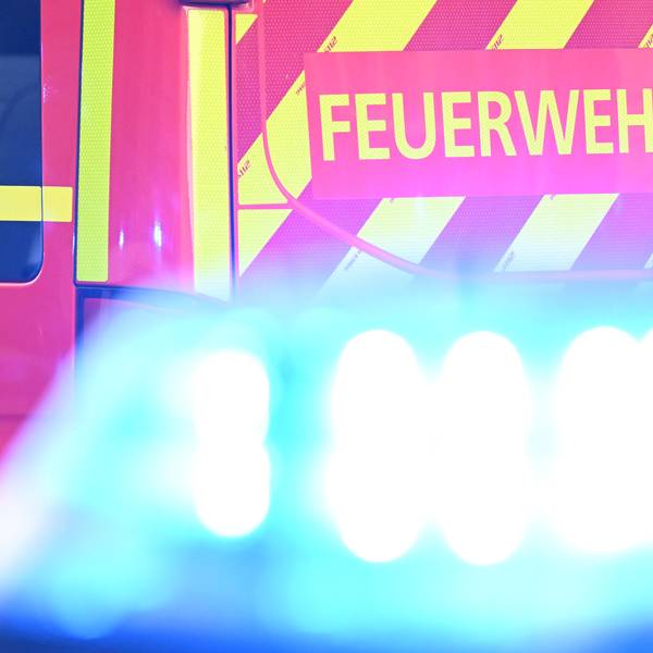 Ein Fahrzeug der Feuerwehr steht bei einem Einsatz auf einer Straße, während im Vordergrund das Blaulicht eines Polizeifahrzeugs zu sehen ist.