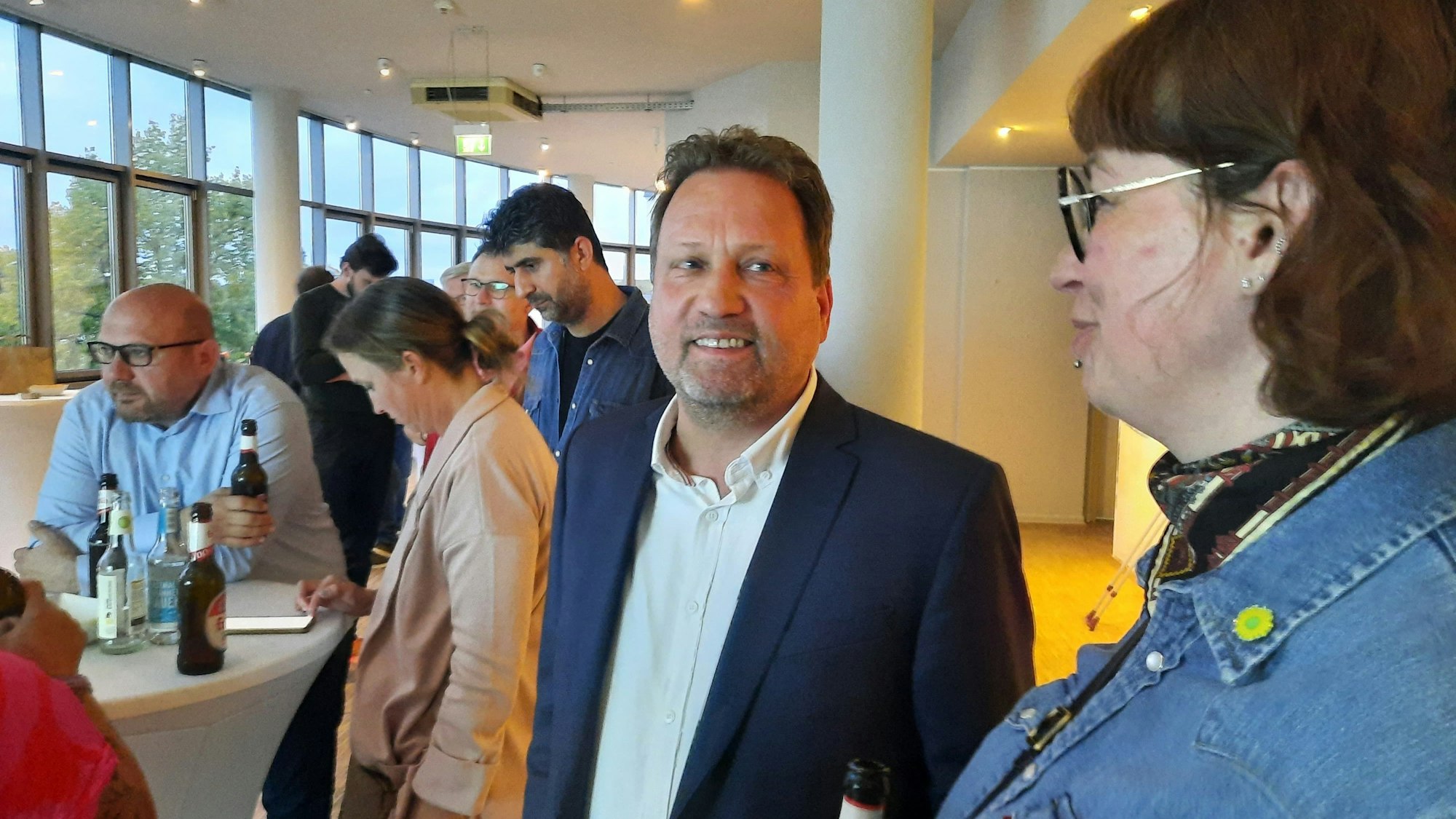 Ein Mann und eine Frau, im Hintergrund mehrere Personen an einem Stehtisch.