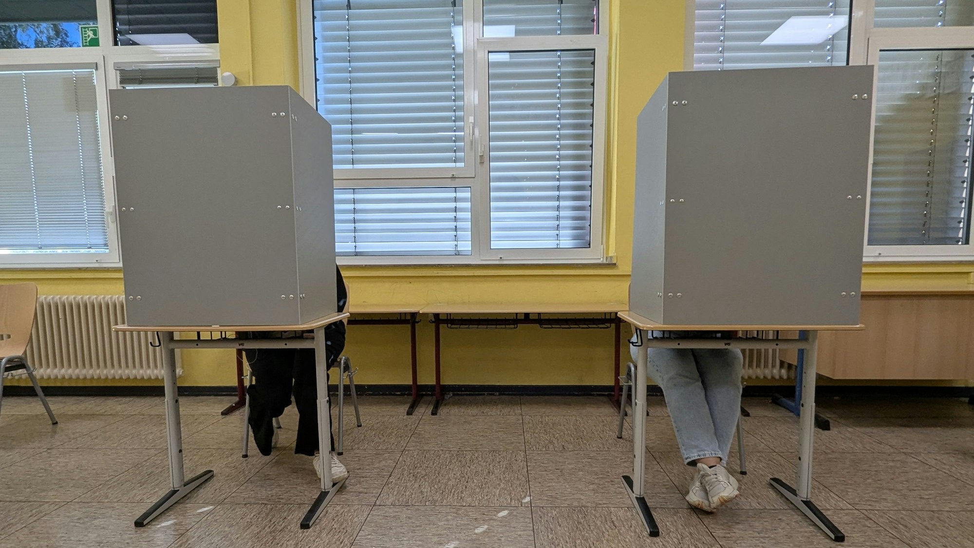 Das Foto zeigt die Beine von zwei Wählenden in Wahlkabinen in Hürth.
