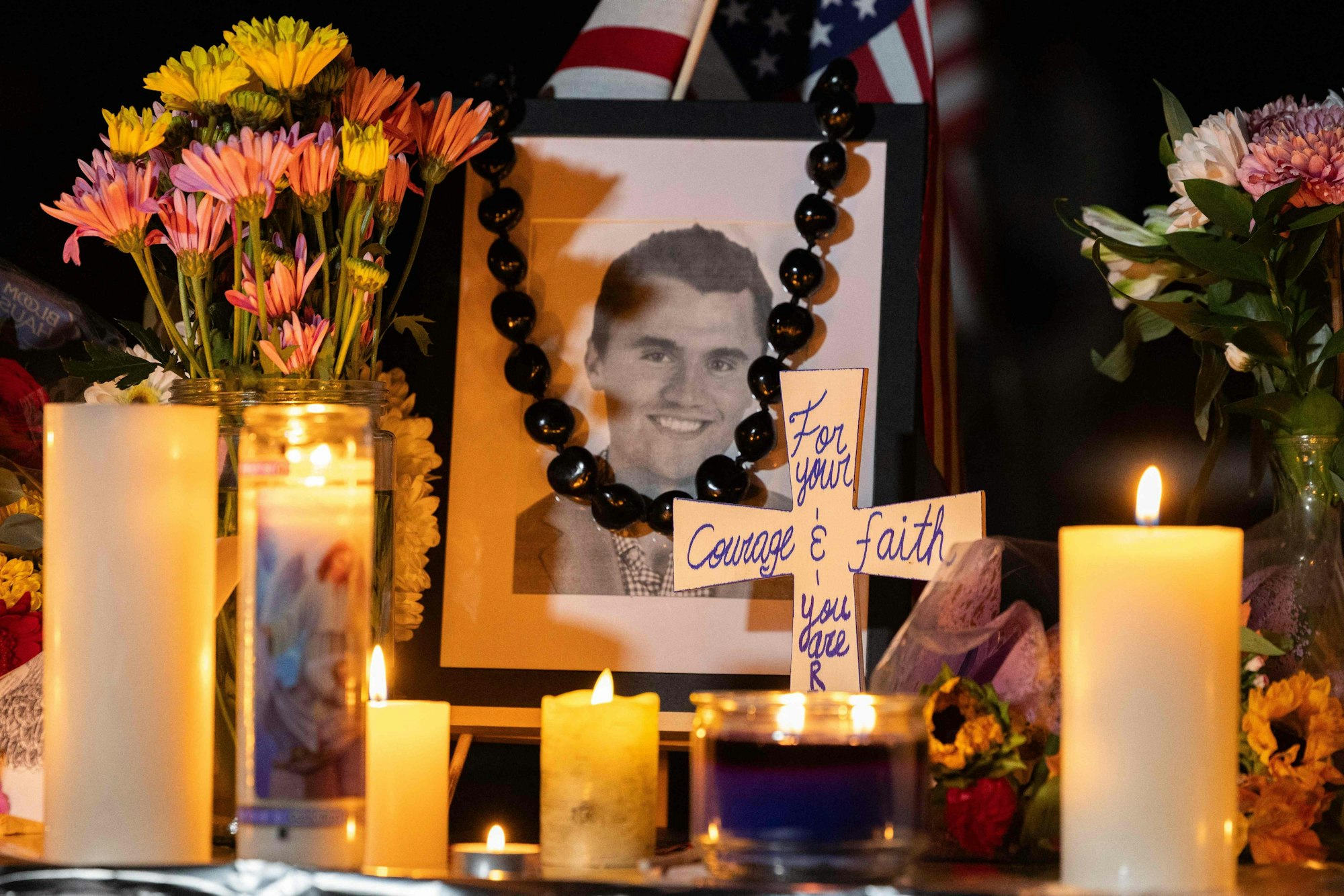 Candles and flowers are seen near a portrait of right-wing activist Charlie Kirk at a makeshift memorial during a candlelight vigil at Memorial Park in Provo, Utah, on September 12, 2025, after he was shot during a public event at Utah Valley University. The widow of prominent right-wing activist Charlie Kirk pledged on September 12 to carry on her husband's work, after US authorities announced his alleged assassin had finally been captured. The 31-year-old Kirk was hit by a single bullet while addressing a large crowd at Utah Valley University in the town of Orem on September 10. (Photo by Melissa MAJCHRZAK / AFP)