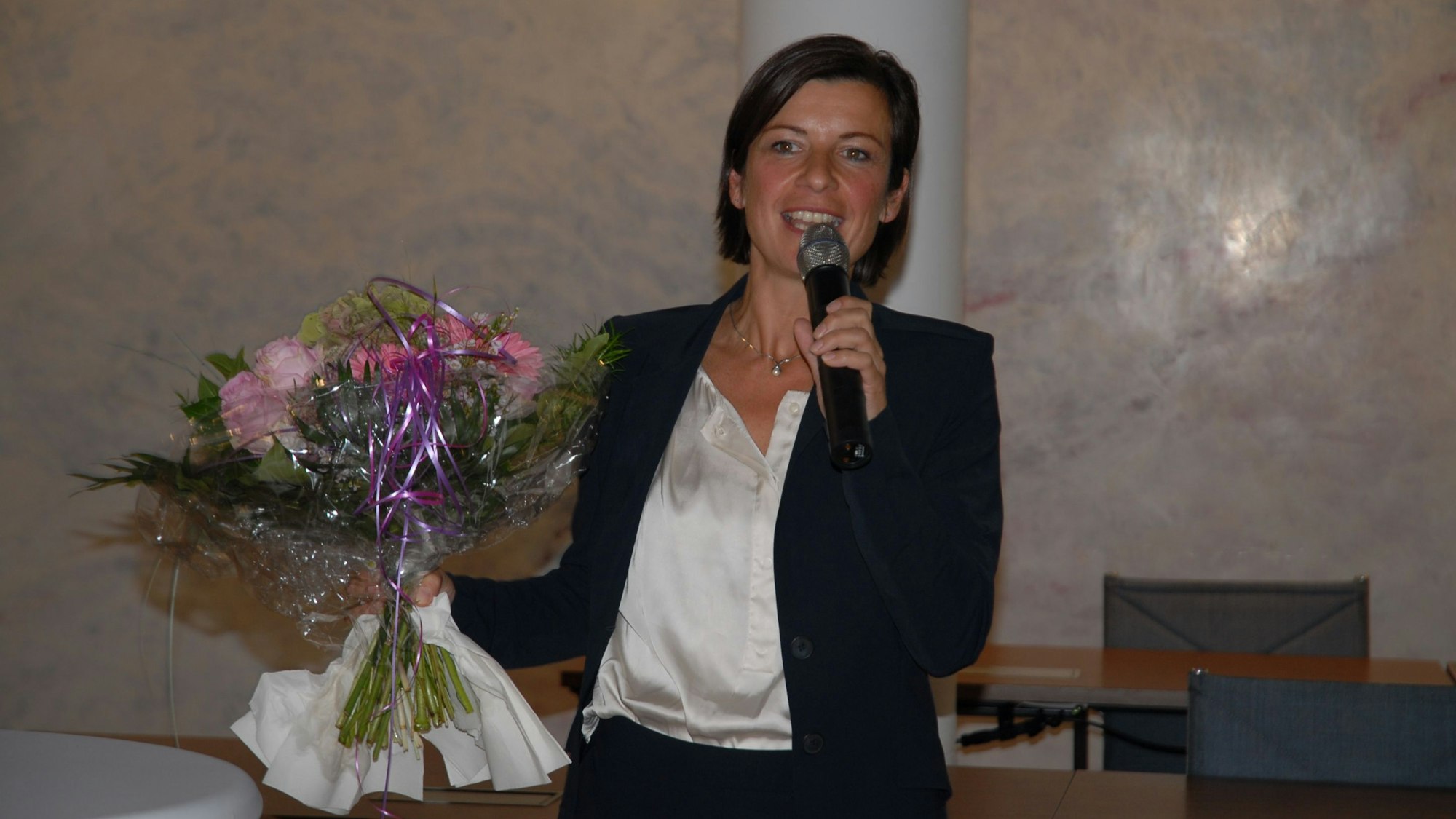 Eine Frau hält einen Blumenstrauß und spricht in ein Mikro.