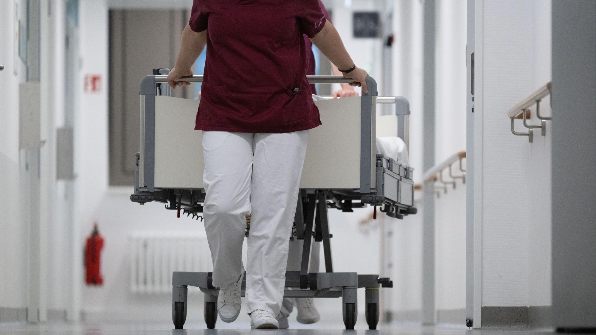Eine Krankenpflegerin und ein Krankenpfleger schieben ein Krankenbett durch den Gang einer Station eines Krankenhauses (Symbolbild)
