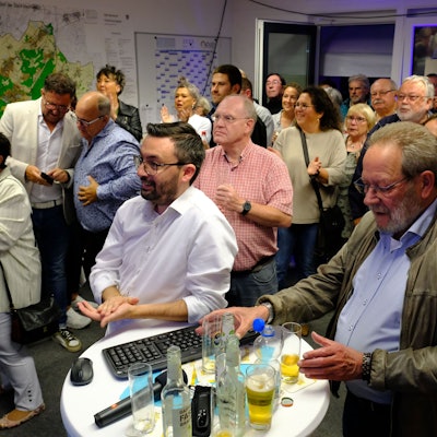 Zahlreiche Menschen stehen bei einer Wahlparty im Mechernich Rathaus in einem Raum.