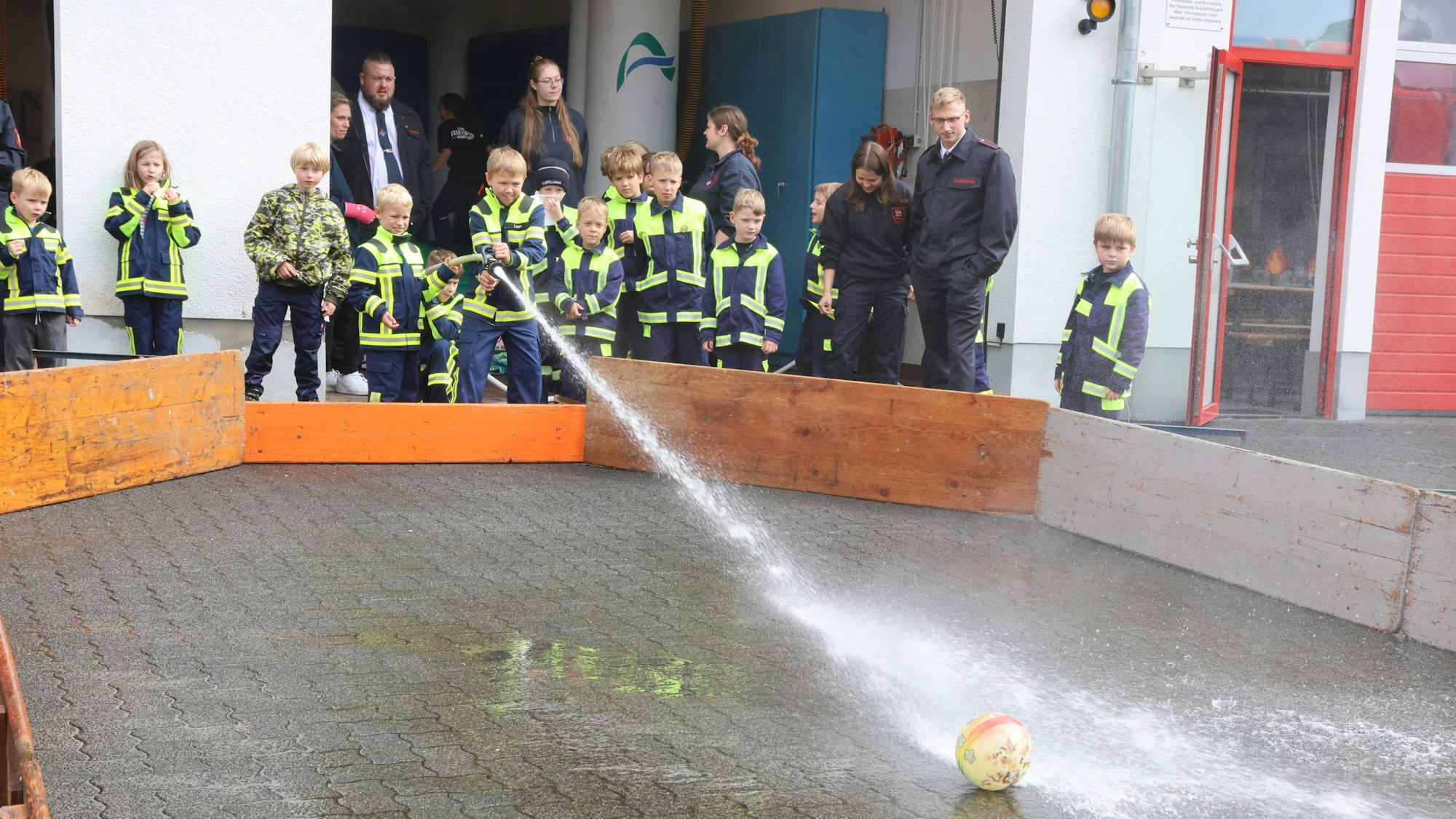 Eine Wasserfußball-Aktion bei einem Fest der Kinderfeuerwehr. Ein Junge spritzt mit Löschwasser aus einem Schlauch auf einen Fußball.