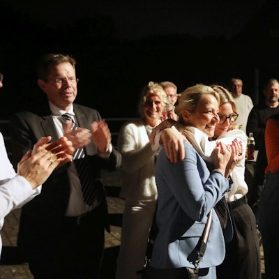 Zwei Frauen umarmen sich, mehrere Menschen applaudieren.