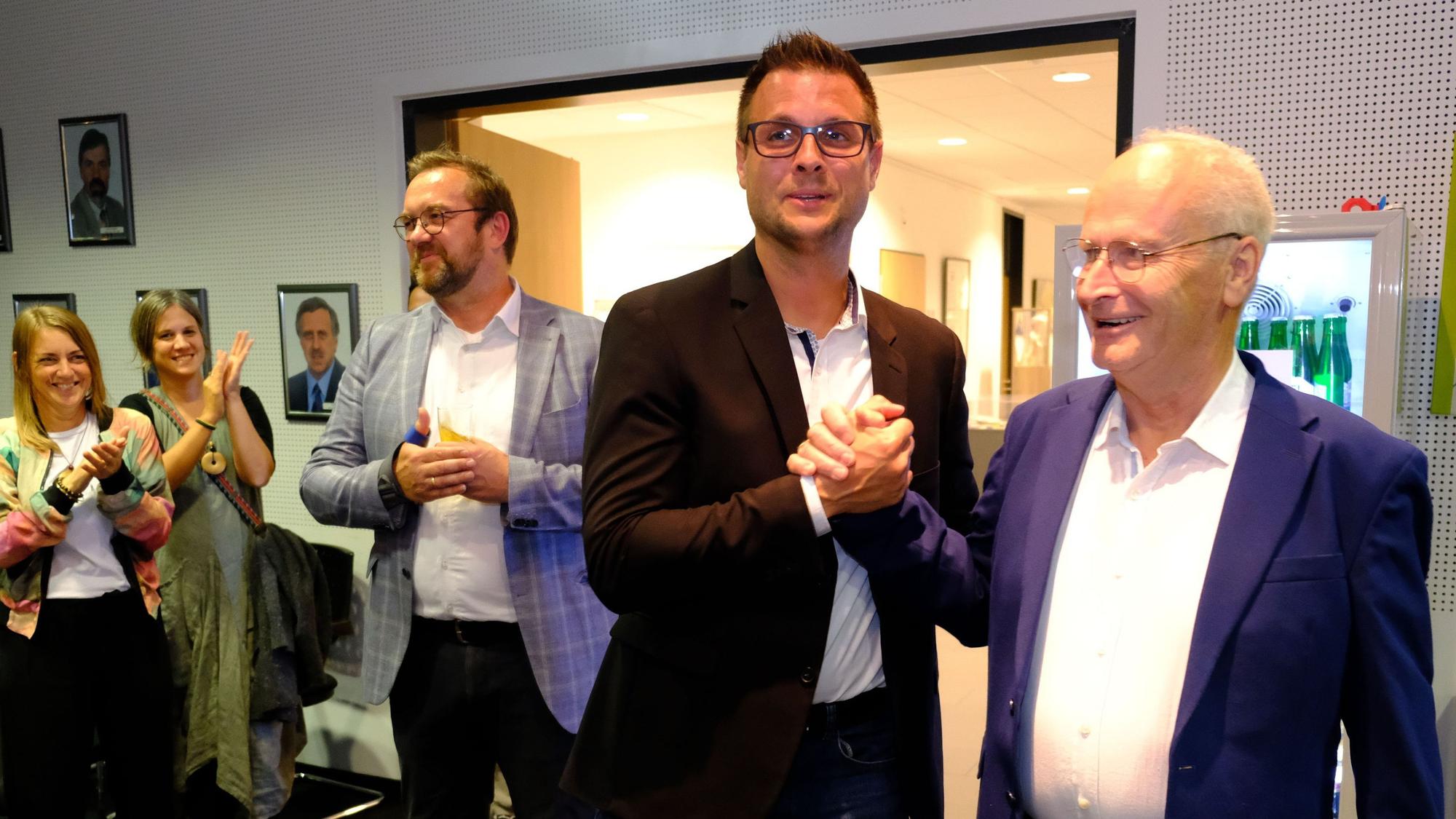 Hans-Peter Schick (r.) gratuliert Michael Fingel per Handschlag. Daneben stehen einige Personen und applaudieren.