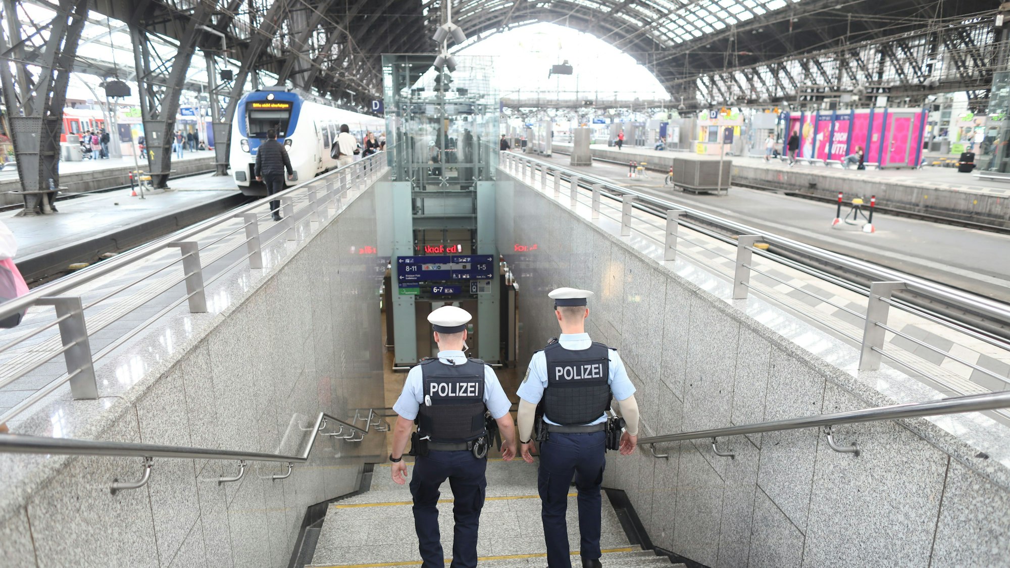 Zwei Bundespolizisten laufen im Kölner Hauptbahnhof eine Treppe hinab. Im oberen Bereich ist das Dach des Bahnhofs zu erkennen.