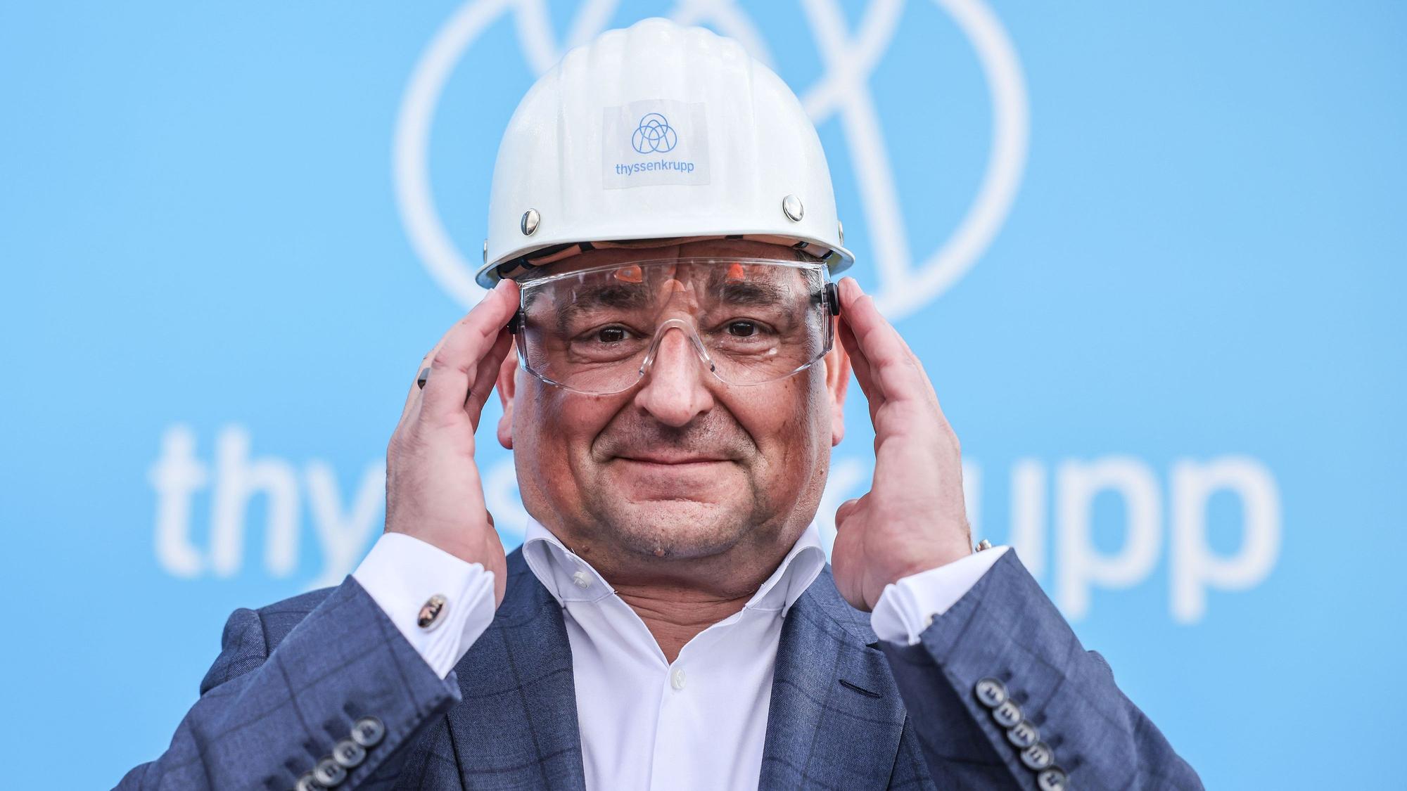 Miguel López steht vor dem Logo des Unternehmens. Er trägt einen Bauhelm.