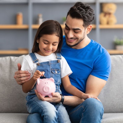 Vater und Tochter füttern gemeinsam das Sparschwein.