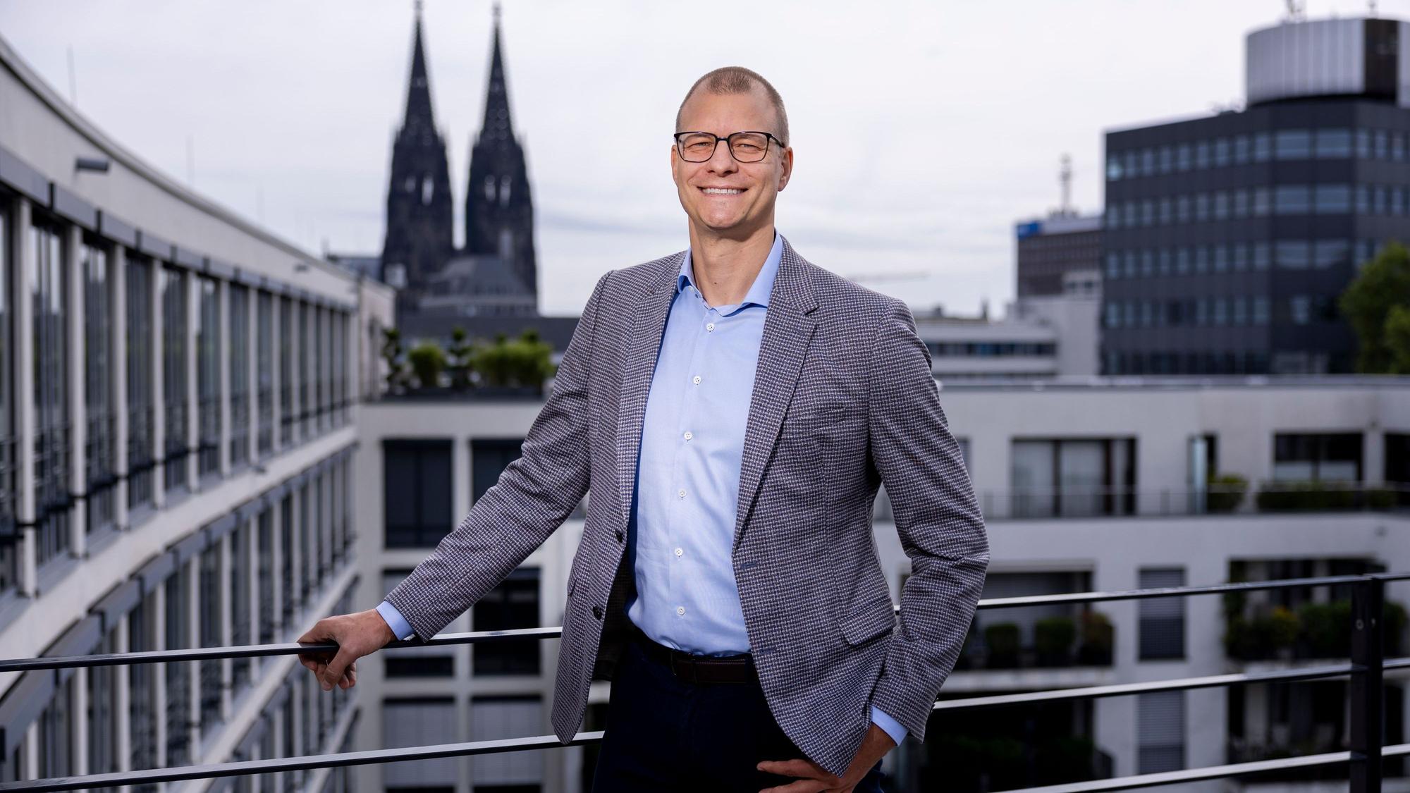 Fabian Spindler steht auf einer Dachterrasse mit Blick auf den Dom.