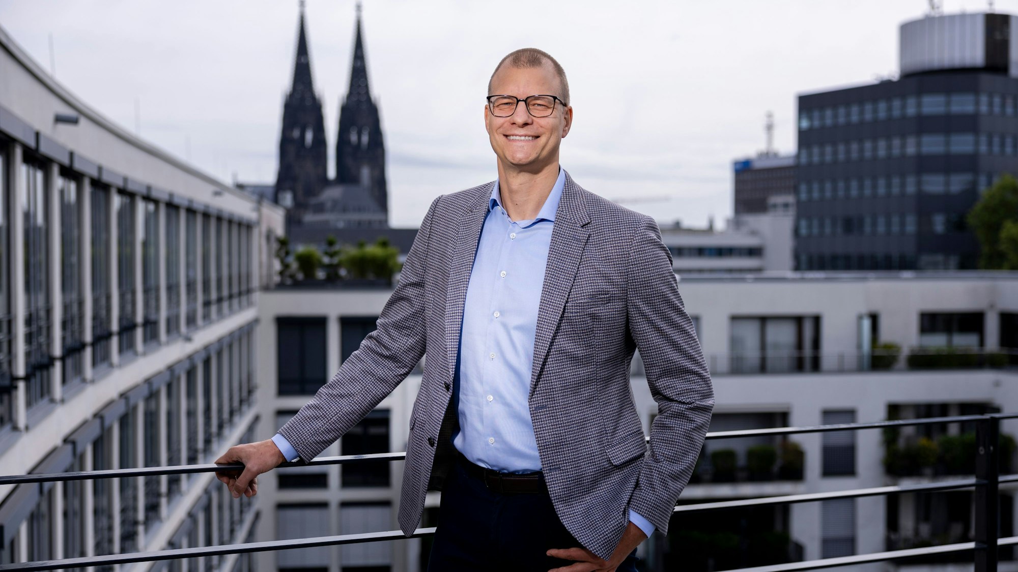 Fabian Spindler steht auf einer Dachterrasse mit Blick auf den Dom.