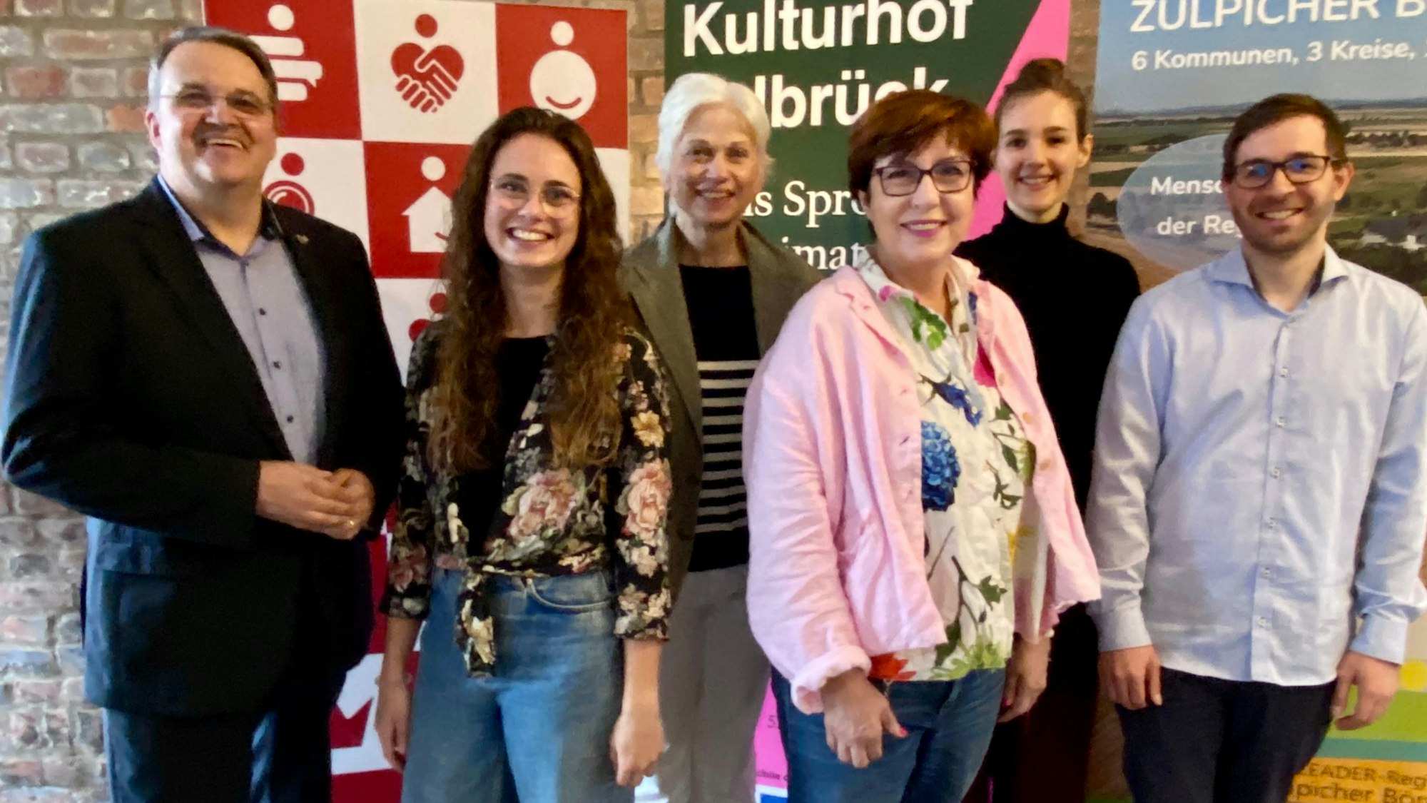 Zwei Männer und vier Frauen stehen nebeneinander und lächeln in die Kamera.