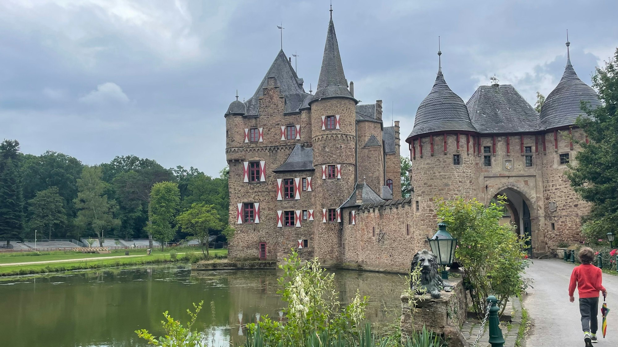 Burg Satzvey mit Weiher davor, ein Kind läuft auf den Eingang zu.