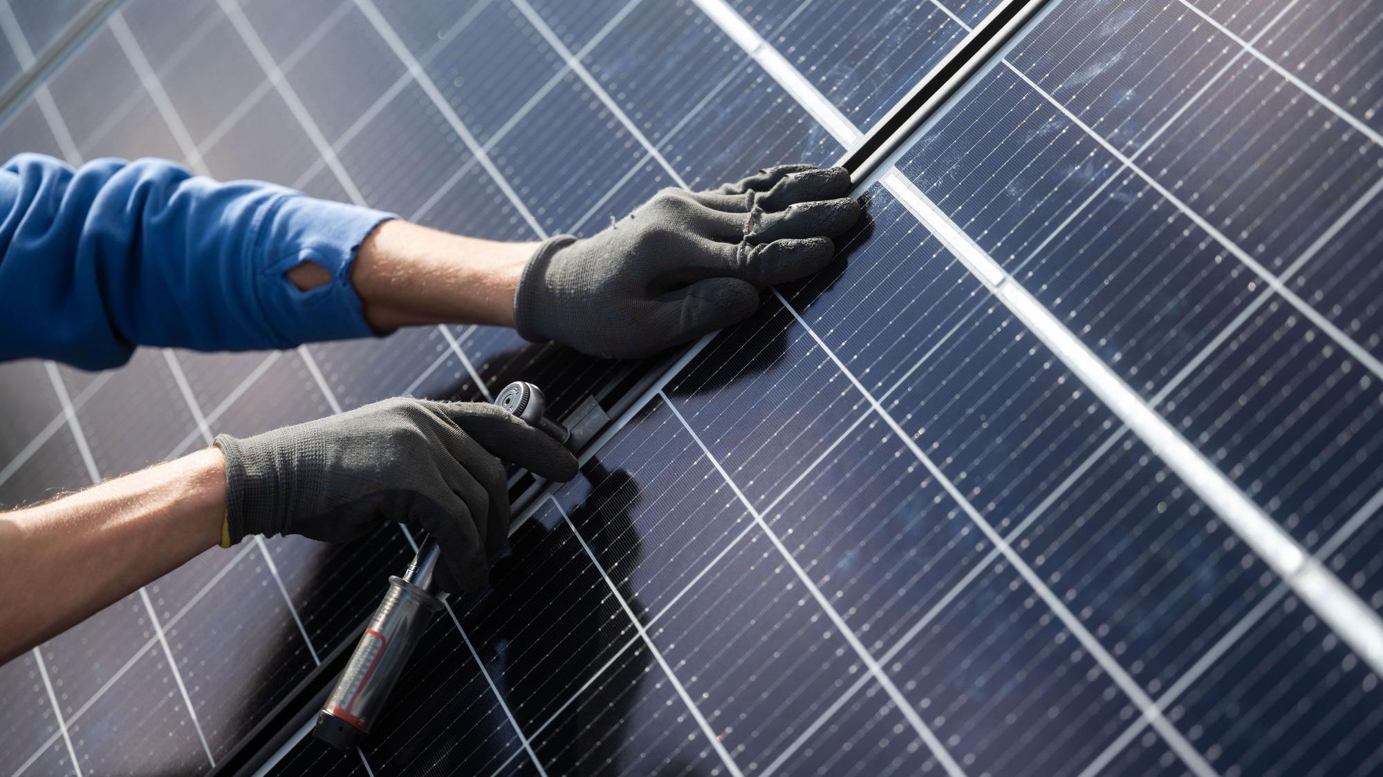 Ein Mann montiert Photovoltaikmodule auf dem Dach eines Wohnhauses. (Archiv)