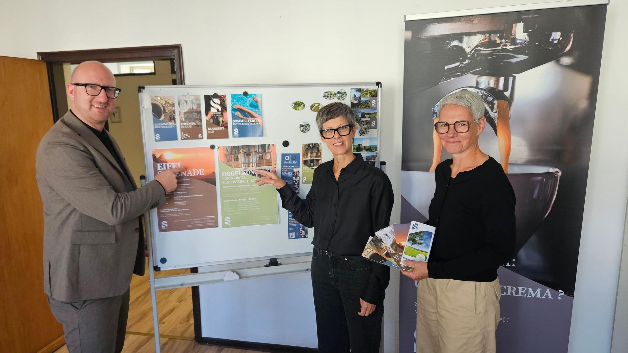 Bürgermeister Ingo Pfennings, Bianka Renn und Stefanie Hermes stehen vor einer Stellwand mit Werbeplakaten von den Veranstaltungen.