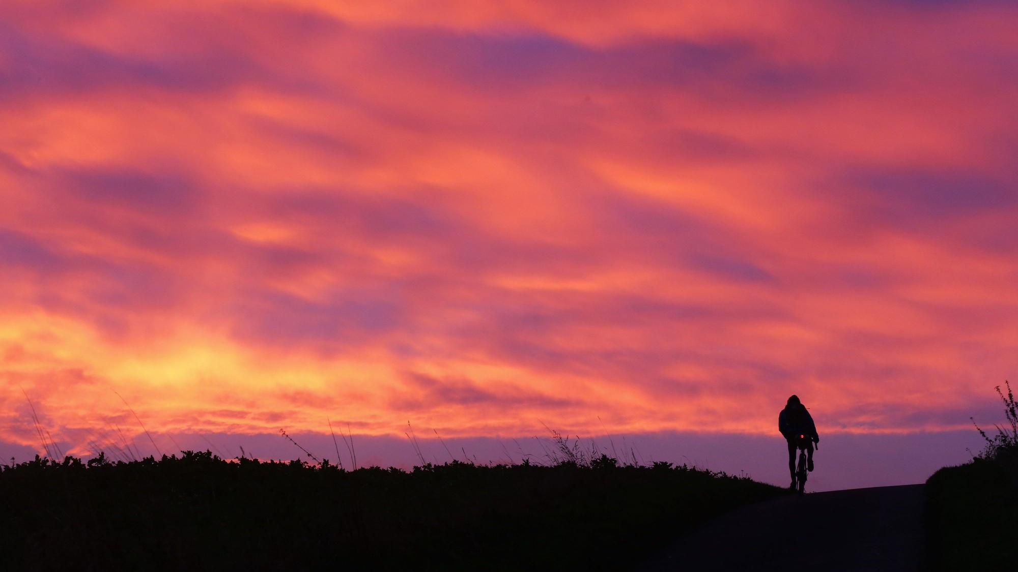 Bei Sonnenaufgang fährt ein junger Mann mit dem Fahrrad auf einem Weg.