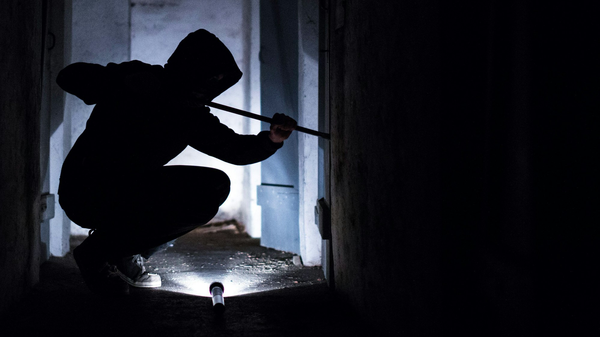 Ein Mann hebelt mit einem Brecheisen eine Tür im Keller eines Wohnhauses auf (gestellte Szene).