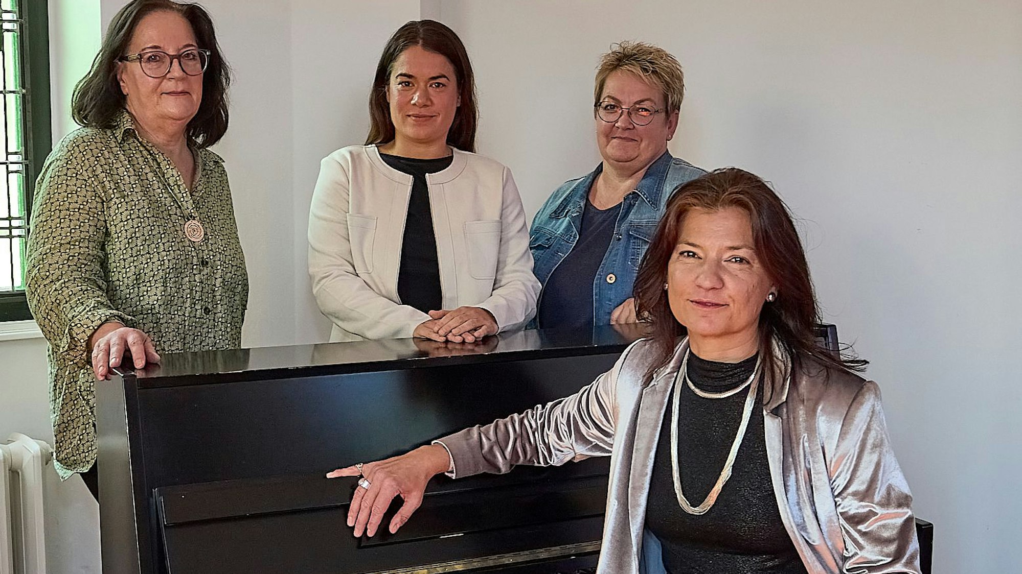 Eine Frau im silbernen Glitzer-Outfit sitzt am Klavier, drei andere Frauen haben sich dahinter postiert, alle schauen in die Kamera.