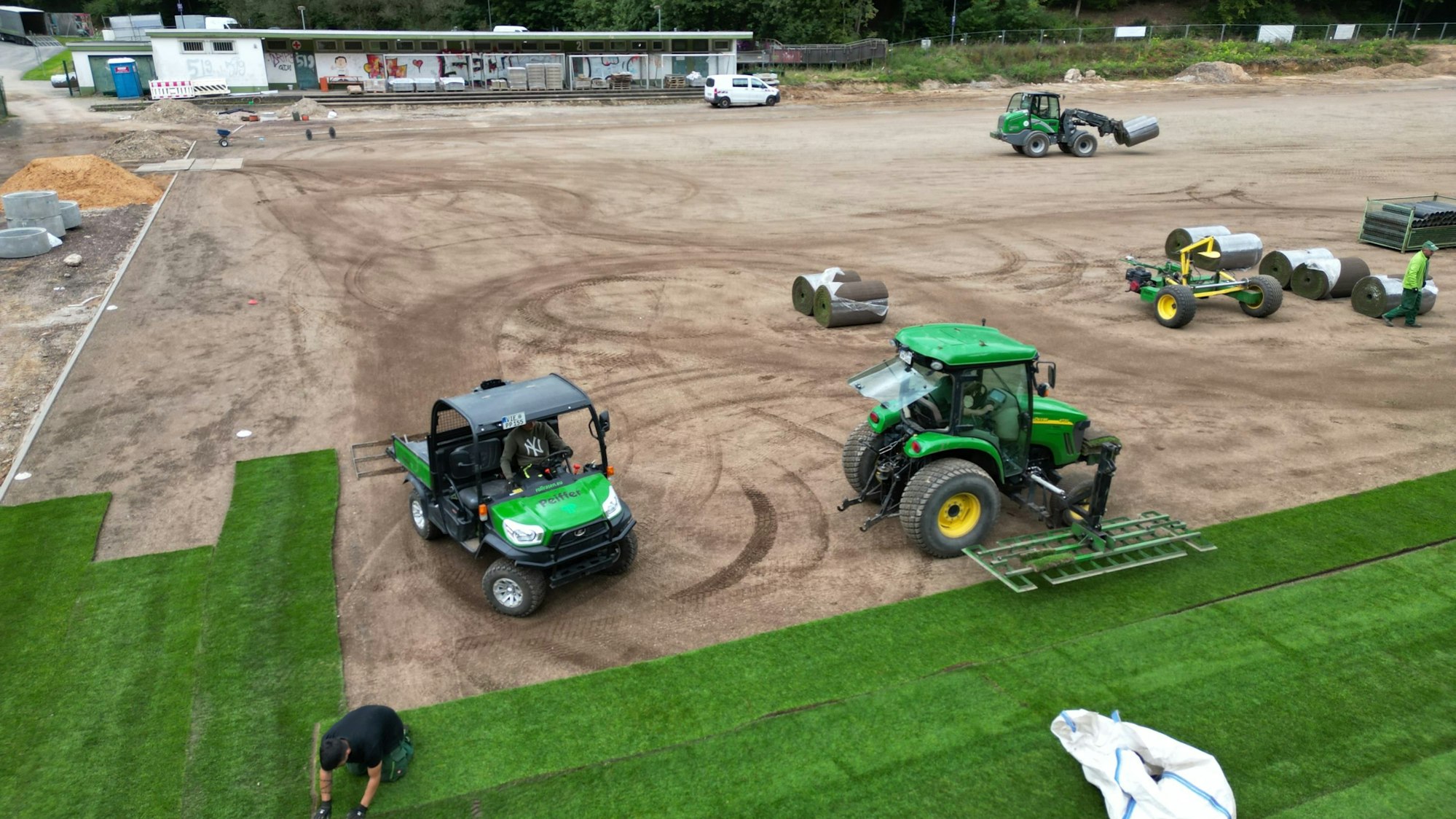 Eine Firma verlegt Rollrasen auf einem Sportplatz.