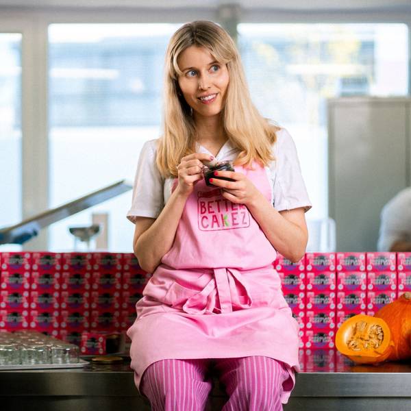 Isabell Forster sitzt auf einer Arbeitsfläche. Sie trägt eine rosafarbene Schürze und löffelt Kuchen aus einem Glas.