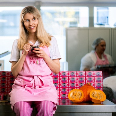 Isabell Forster sitzt auf einer Arbeitsfläche. Sie trägt eine rosafarbene Schürze und löffelt Kuchen aus einem Glas.