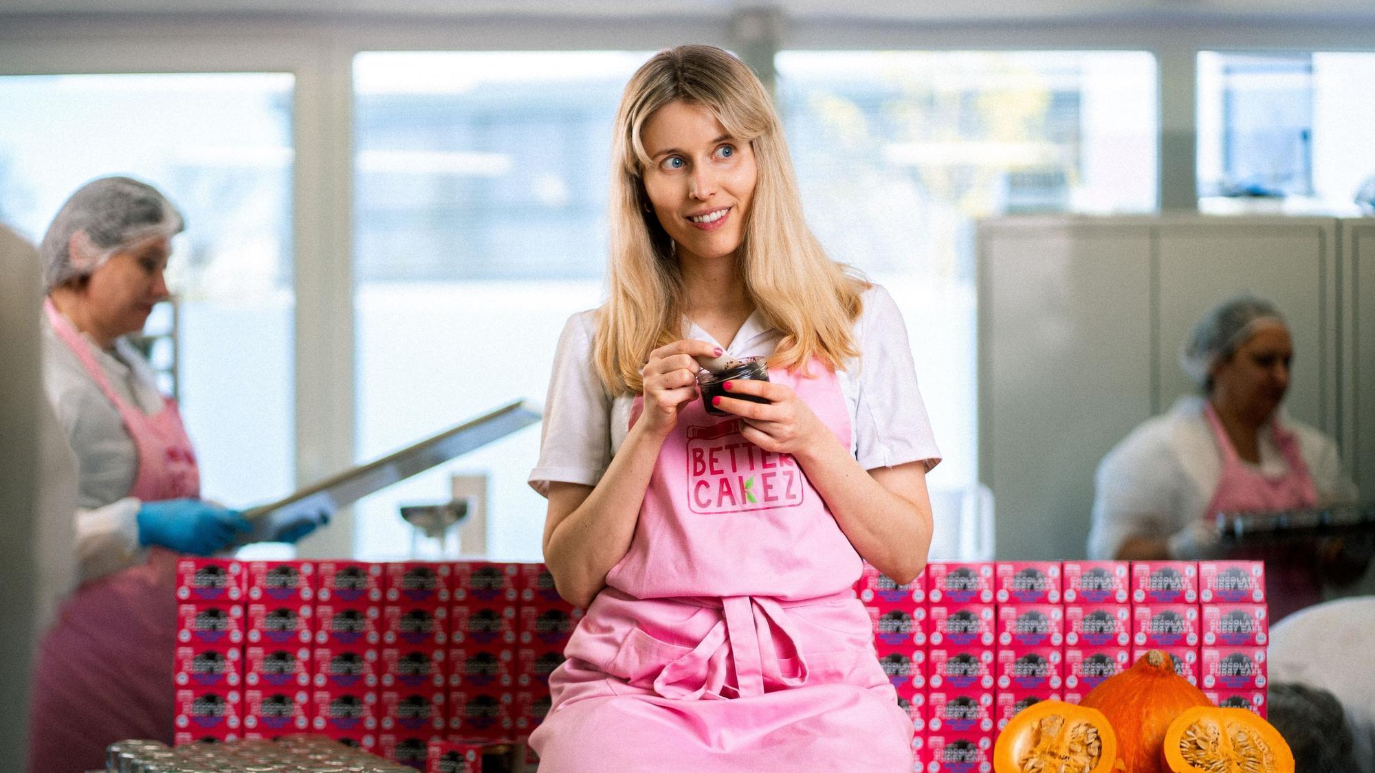 Isabell Forster sitzt auf einer Arbeitsfläche. Sie trägt eine rosafarbene Schürze und löffelt Kuchen aus einem Glas.