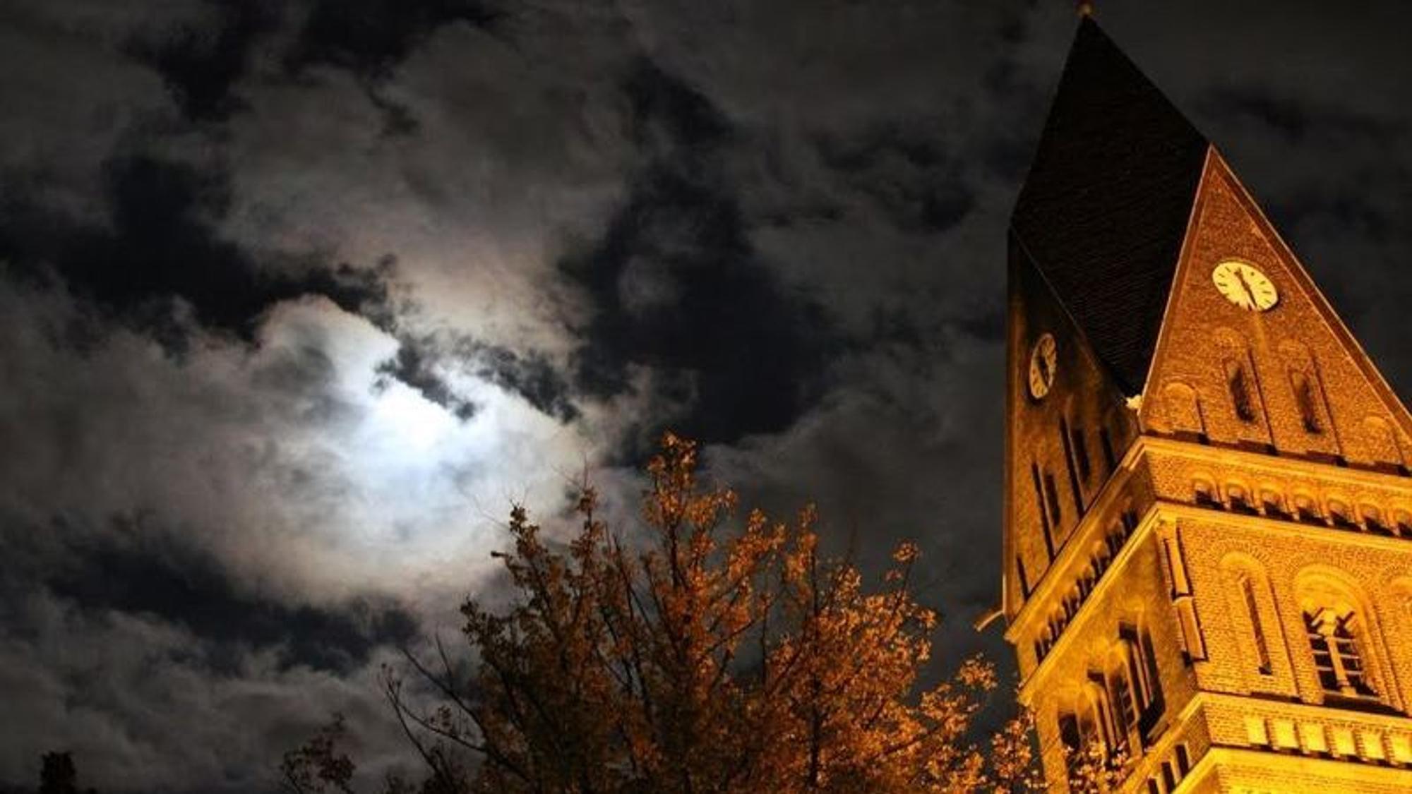 Ein angestrahlter Kirchturm bei Nacht ist zu sehen.
