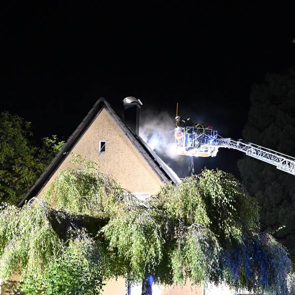 Aus dem Dach eines Hauses kommt Rauch, eine Drehleiter ist im Einsatz.