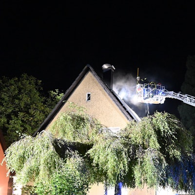 Aus dem Dach eines Hauses kommt Rauch, eine Drehleiter ist im Einsatz.