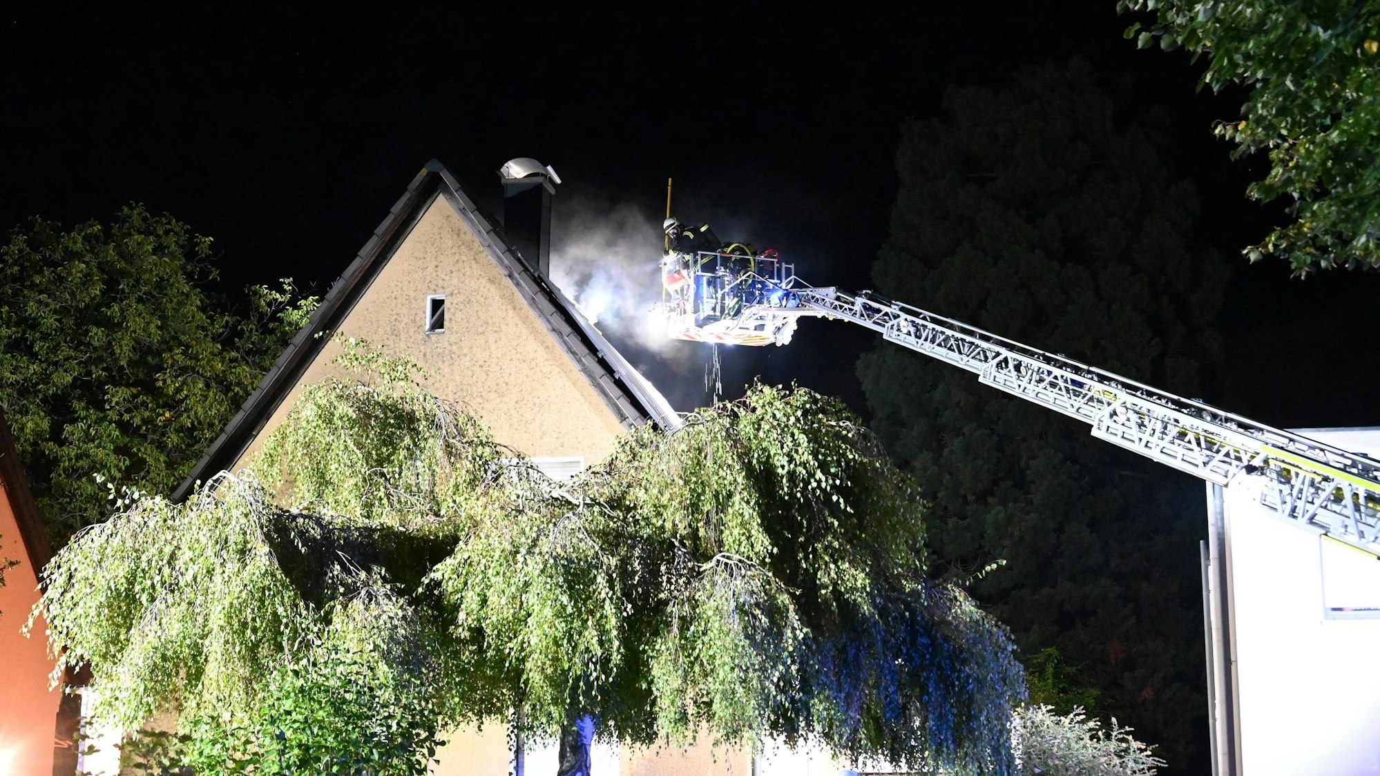 Aus dem Dach eines Hauses kommt Rauch, eine Drehleiter ist im Einsatz.
