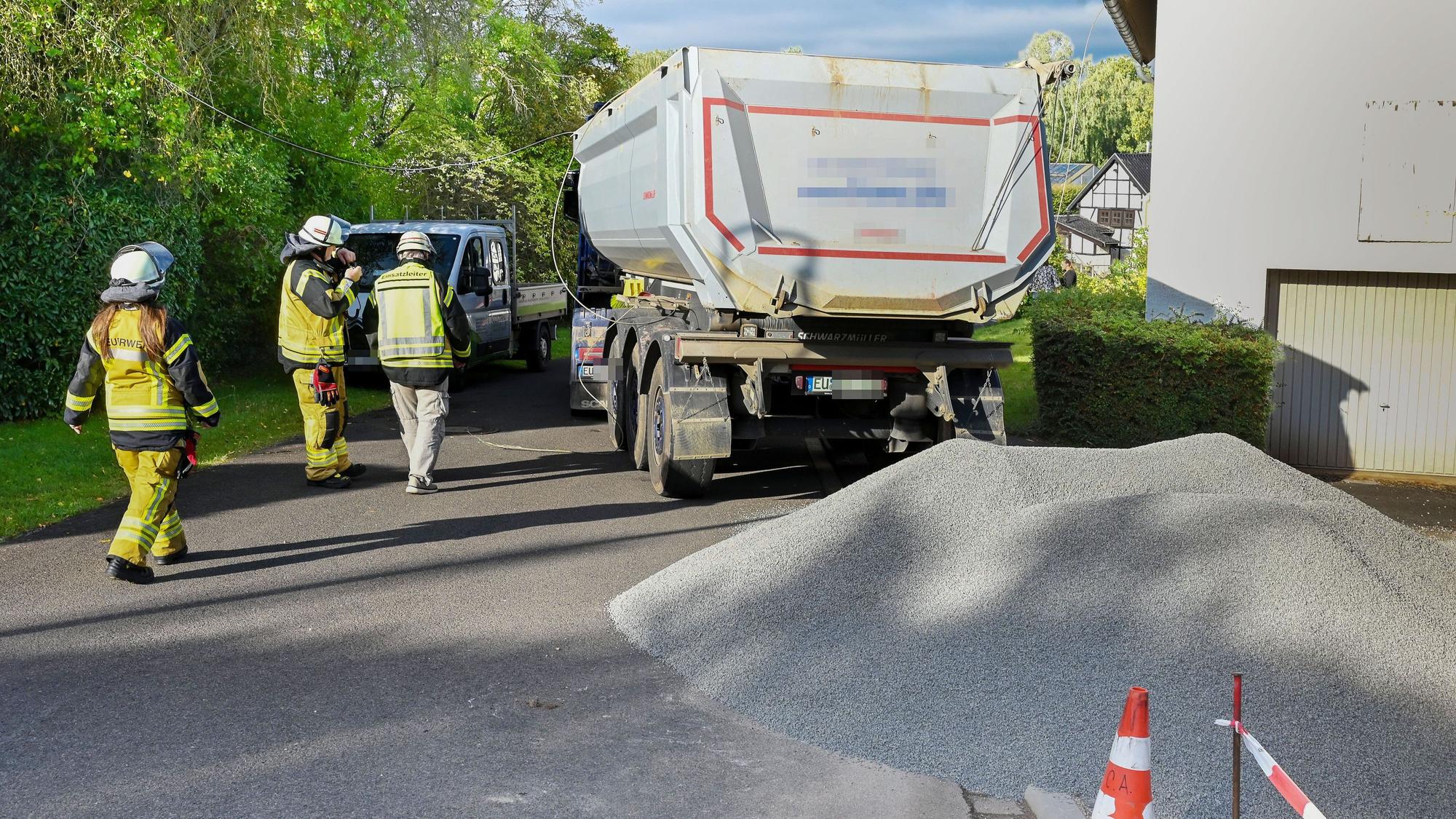 Ein Haufen Splitt liegt auf einer Straße, dahinter steht ein Lastwagen, an dem drei Feuerwehrleute vorbeigehen.