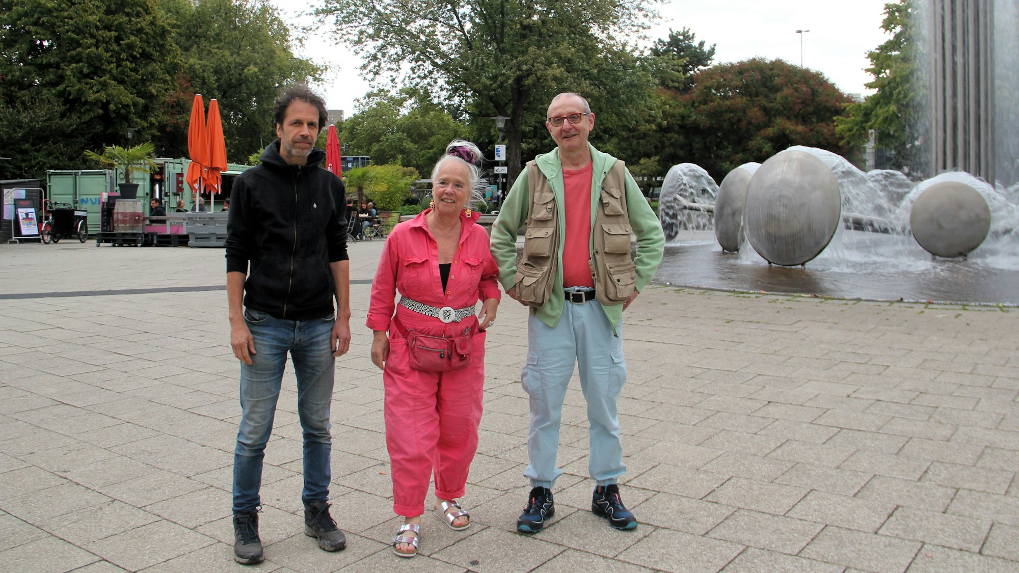 Zwei Männer und eine Frau stehen auf vor dem Brunnen auf dem Ebertplatz.