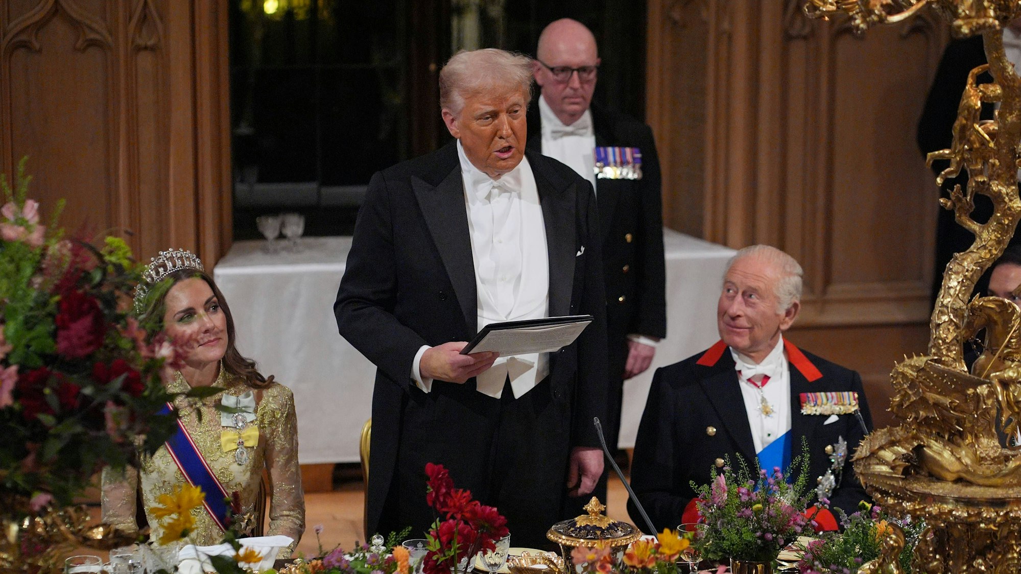 Donald Trump hält beim Staatsbankett im Windsor Castle eine Rede, neben ihm sitzen Prinzessin Kate im goldenen Kleid mit Tiara und König Charles, der ihn anblickt.