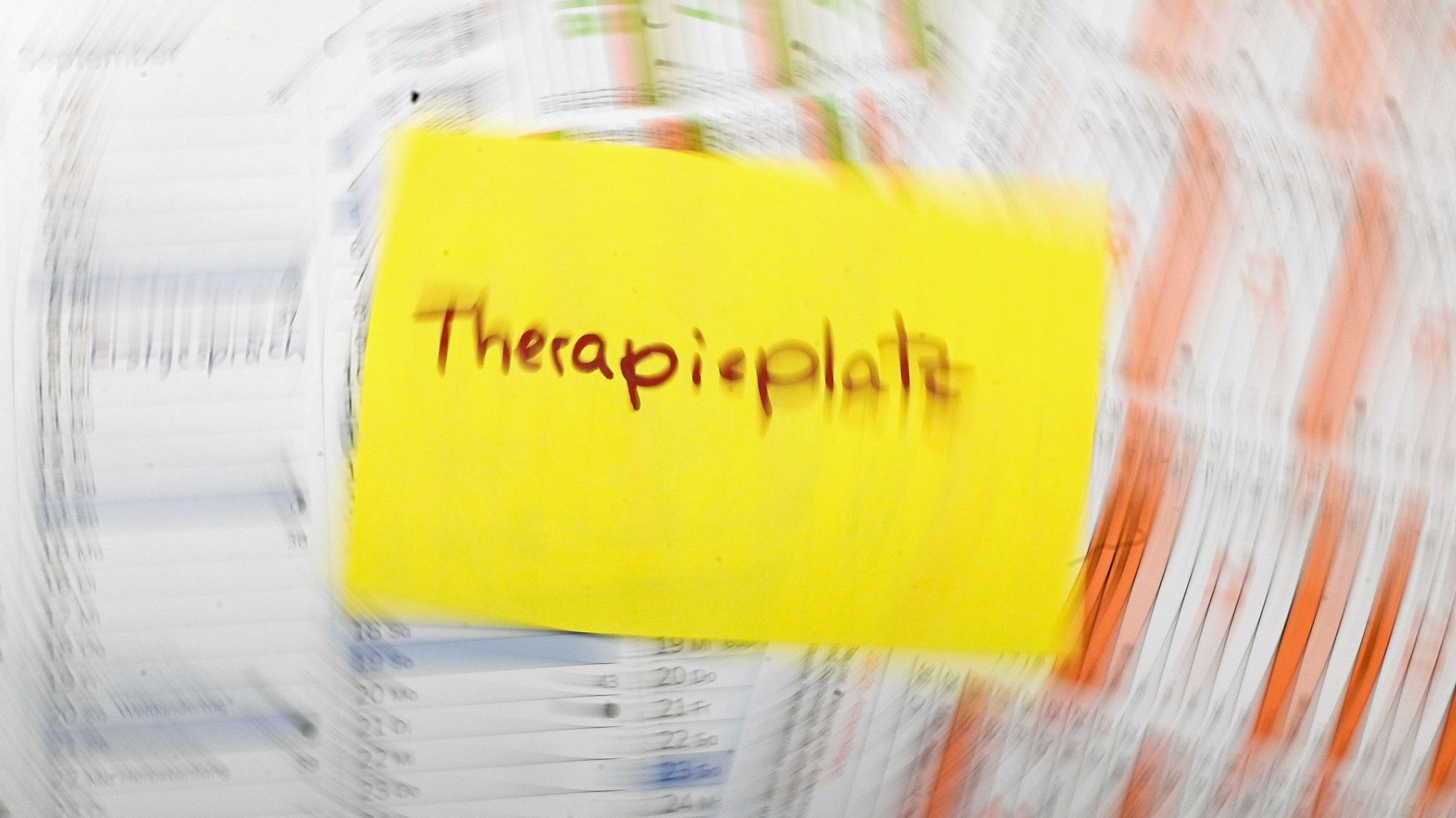 Ein Zettel mit dem Schriftzug ´Therapieplatz» liegt auf mehreren Monatskalendern. (Aufnahme mit langer Verschlusszeit und Zoom-Effekt)