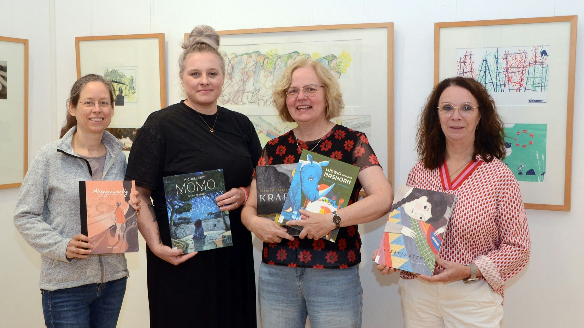 Vier Frauen stehen vor Bildern in einer Ausstellung; sie halten Bilderbücher in der Hand.