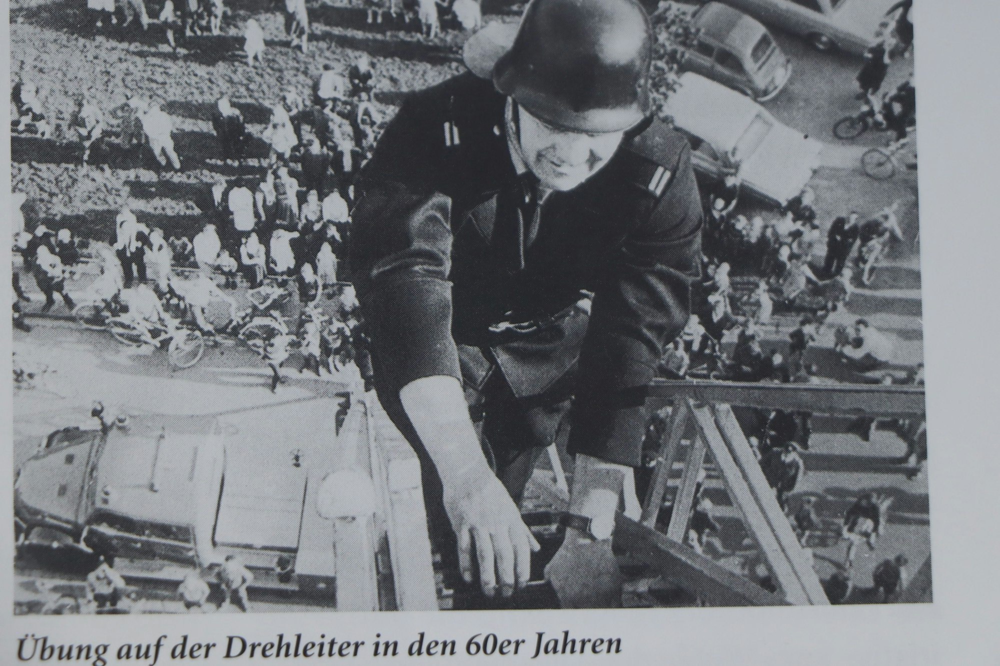 Auf dem Bild ist ein Mann auf einer hohen Drehleiter zu sehen. Viele Menschen schauen von unten zu.