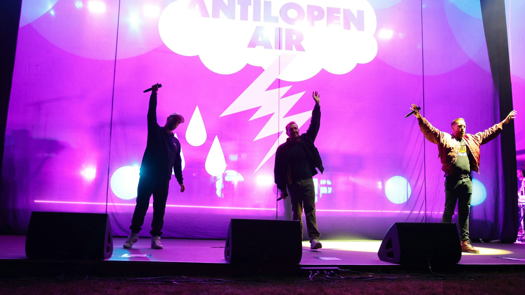 Drei Musiker winken von der Bühne ins Publikum.