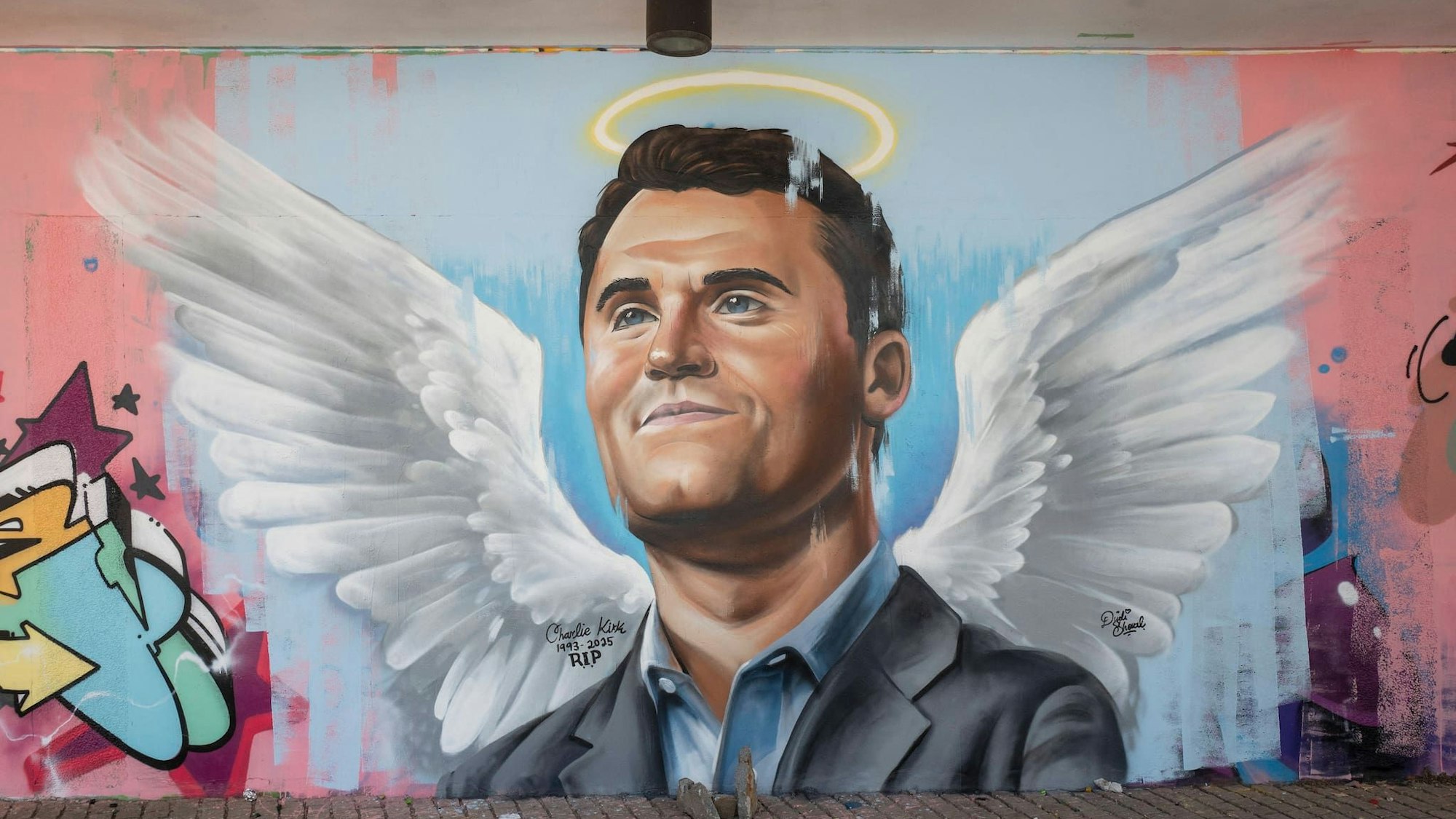 Ein an die Wand gemaltes Bild von Charlie Kirk mit Heiligenschein und Flügeln.