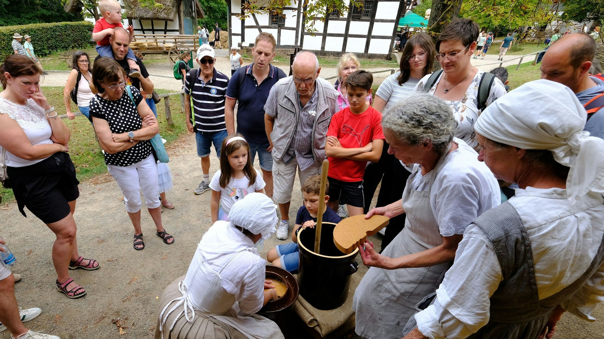 Besucher des Freilichtmuseums schauen den traditionell mit Kopftuch und Schürzen gekleideten Hauswirtschafterinnen bei ihrer Arbeit zu.