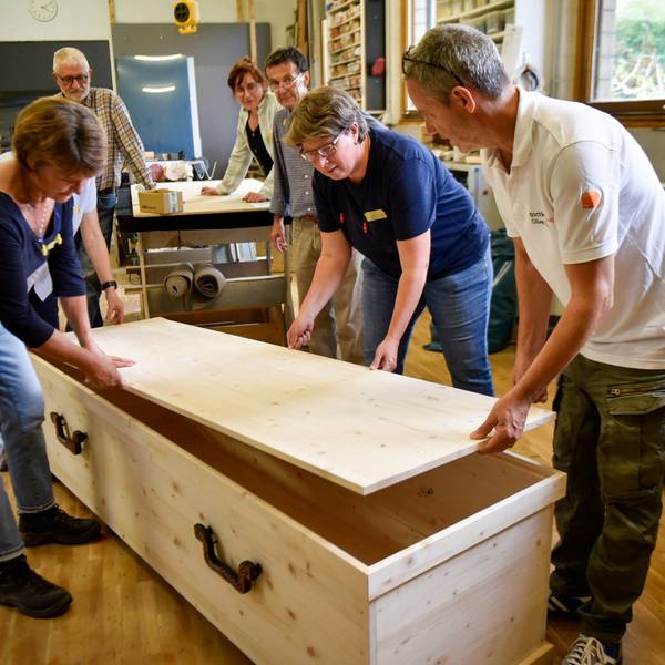 Auf dem Bild sind Teilnehmer eines Workshops mit einem selbst gebauten Holzsarg zu sehen.